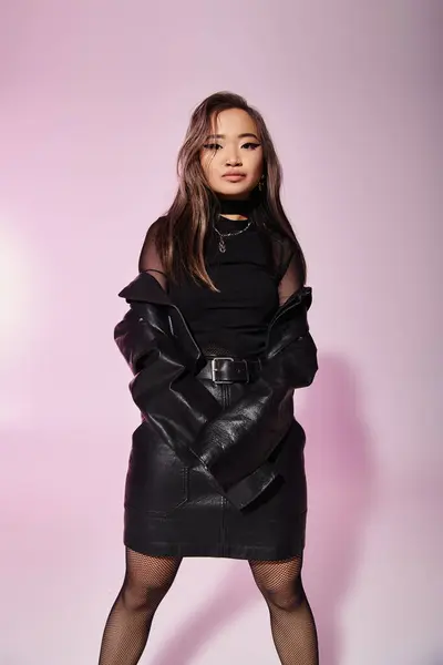 Bonita mujer joven asiática en traje de cuero negro posando sobre fondo lila - foto de stock