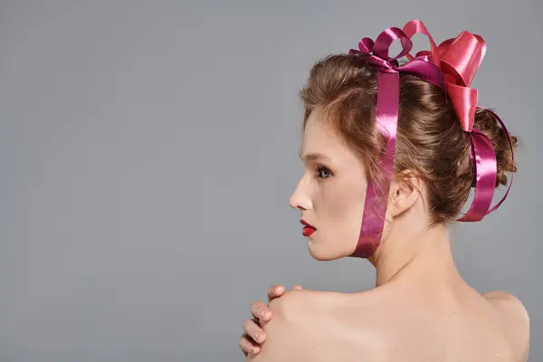 Молода жінка викриває класичну красу, коли вона вдаряє позу з ніжним рожевим бантом, що обожнює волосся в студійній обстановці. — стокове фото