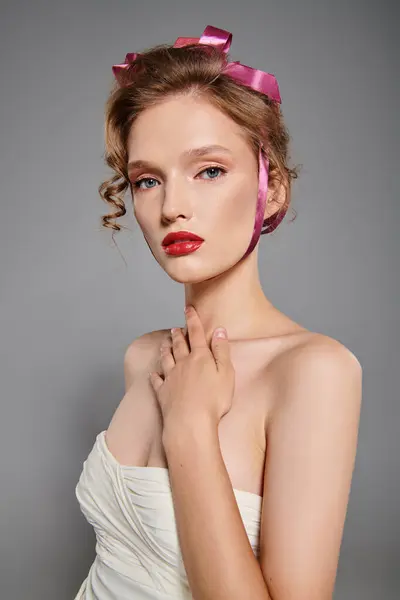 Una giovane donna trasuda bellezza classica mentre posa in un abito bianco con un fiocco rosa sulla testa in un ambiente sereno studio. — Foto stock
