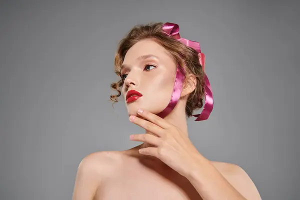 Jeune femme respire la beauté classique alors qu'elle pose en toute confiance avec un arc rose sur la tête dans un décor de studio sur un fond gris. — Photo de stock