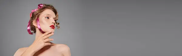 A young woman exudes classic beauty, posing in a studio with a pink bow on her head against a grey backdrop. — Stock Photo