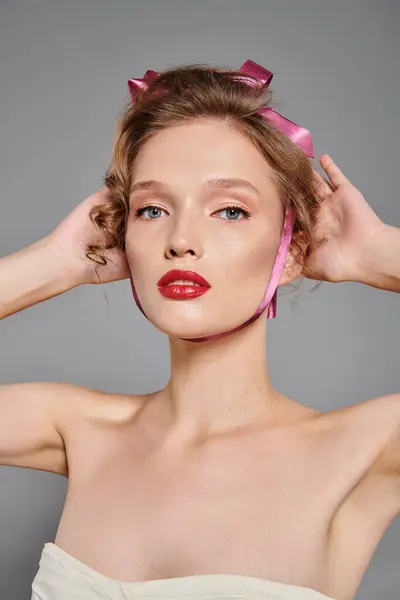 Une jeune femme à la beauté classique pose dans un studio, portant un arc rose sur la tête sur un fond gris. — Photo de stock