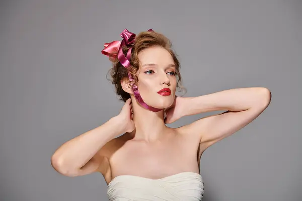 Une jeune femme avec un arc rose dans les cheveux respire la beauté classique tout en prenant une pose dans un cadre de studio. — Photo de stock