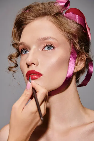 Une beauté classique, une jeune femme pose élégamment avec un arc rose perché sur sa tête dans un studio sur fond gris. — Photo de stock