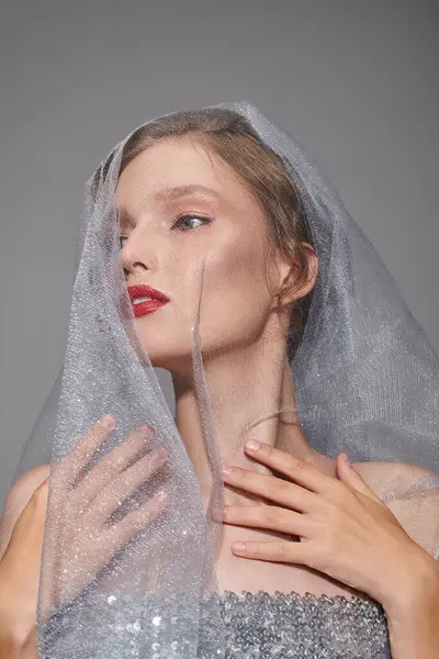 A young woman exudes classic beauty in a studio as she poses with a veil draped over her head. — Stock Photo