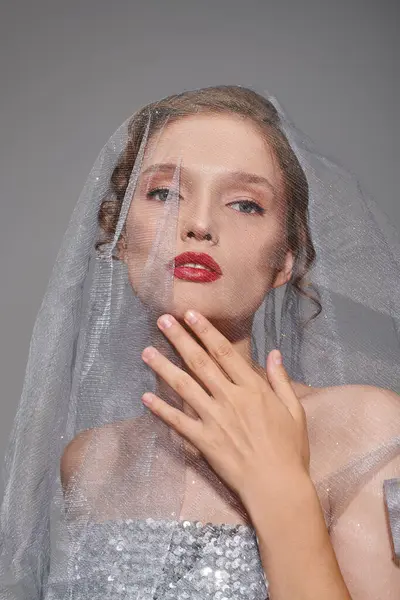 Une jeune femme exsudant une beauté classique, portant un voile et un rouge à lèvres rouge vif dans un décor studio sur fond gris. — Photo de stock