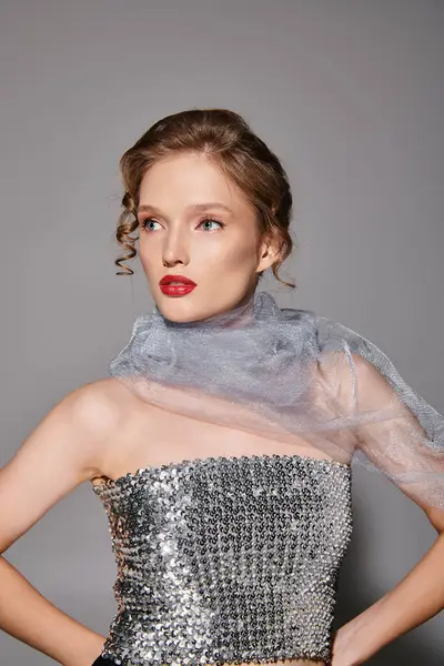 A young woman exudes classic beauty as she strikes a pose in a stunning silver dress and bold red lipstick on a grey backdrop. — Stock Photo