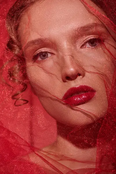 Une jeune femme respire la beauté classique alors qu'elle pose avec un voile rouge ornant sa tête dans un décor de studio. — Photo de stock