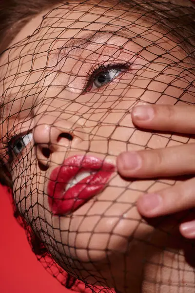 A mysterious woman with red lipstick and a net covering her face exudes classic beauty and intrigue in a studio setting. — Stock Photo