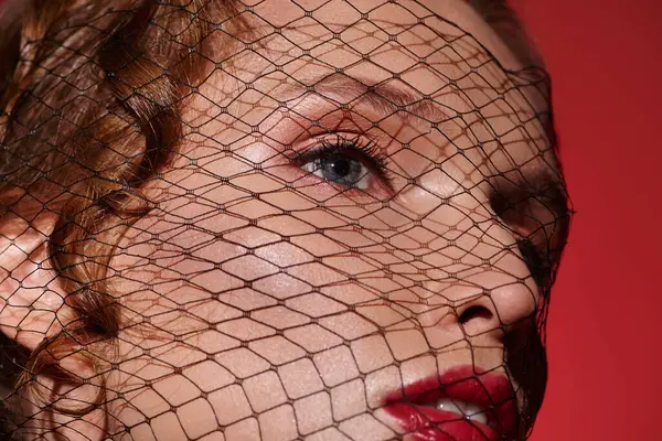 A young woman exudes classic beauty with a red veil covering her face, creating an air of mystery and elegance. — Stock Photo