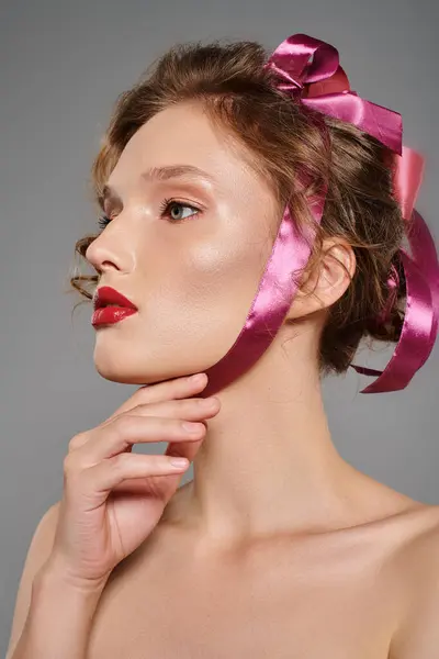A young woman exudes classic beauty while wearing a pink bow on her head in a studio setting against a grey backdrop. — Stock Photo