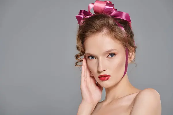 A young woman exudes classic beauty while posing in a studio, wearing a pink bow on her head against a grey backdrop. — Stock Photo