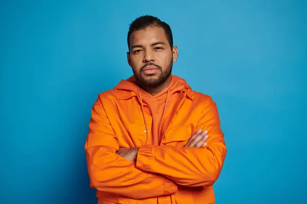 Selbstbewusster afrikanisch-amerikanischer Mann in orangefarbenem Outfit blickt mit gefalteten Kreuzarmen in die Kamera — Stockfoto