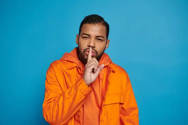 Attractive african american man in orange outfit showing hush gesture silence on blue background — Photo de stock