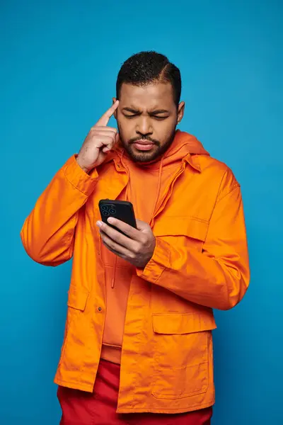 Thoughtful african american man in orange outfit scrolling in social media and touching to temple — Stock Photo