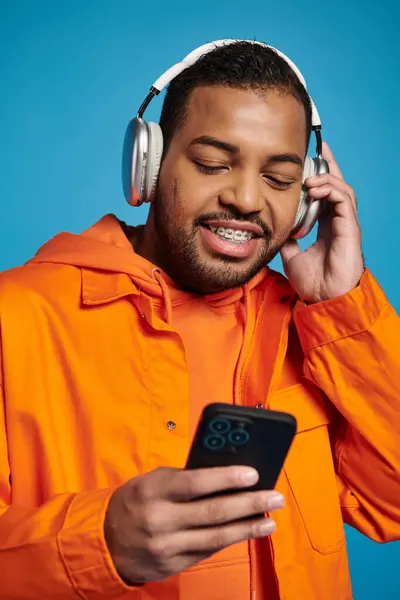 Happy african american man in orange outfit and headphones listening to music with smartphone — Stock Photo