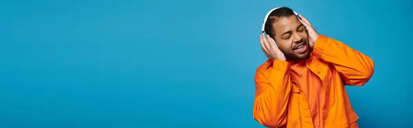 Banner of african american man in his 20s listening to music and holding with hands on headphones — Stock Photo