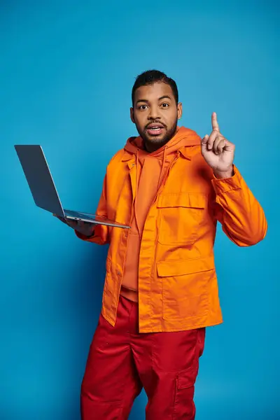 Carismático hombre afroamericano en traje naranja con portátil se le ocurrió una idea sobre fondo azul - foto de stock