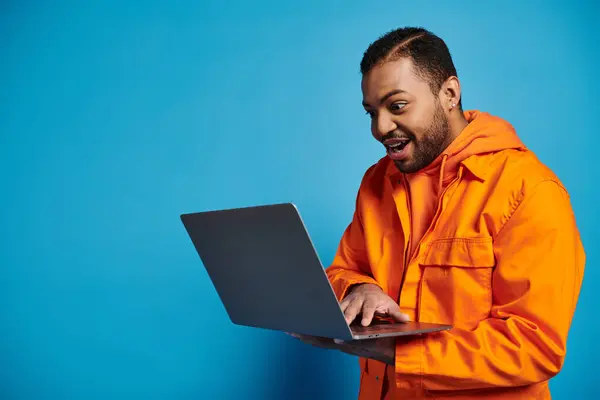 Joyful african american young man in orange outfit enthusiastically playing in videogame in laptop — Photo de stock