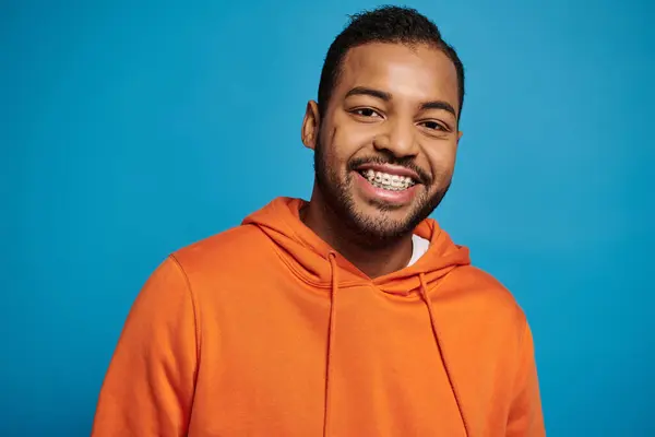 Красивий афроамериканський молодий чоловік в помаранчевому вбранні широко посміхається на синьому фоні — стокове фото