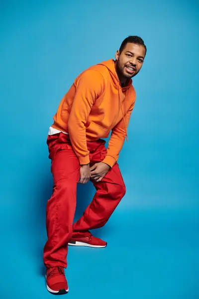 Bel homme afro-américain en tenue vibrante penché et accroupi sur fond bleu — Photo de stock