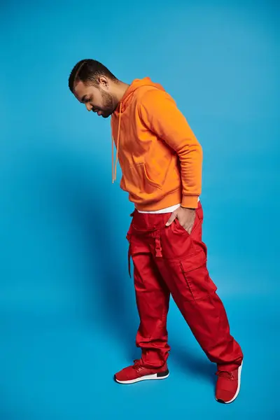 Young african american man in vibrant outfit looking on floor against blue background — Stock Photo