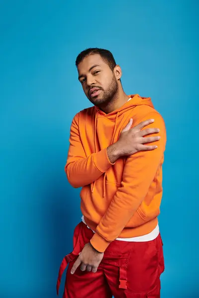 Charismatic african american man in vibrant outfit holding shoulder on blue background — Stock Photo