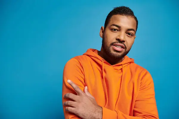 Portrait of attractive african american young man in orange hoodie against blue background — Stock Photo