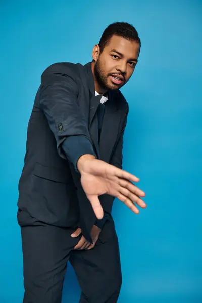 Encantador hombre afroamericano en trajes de color azul oscuro que se esconden de la cámara con la mano sobre fondo azul - foto de stock
