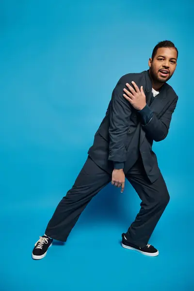 Hombre afroamericano guapo en traje azul oscuro sosteniendo la mano en el hombro y inclinándose a un lado - foto de stock