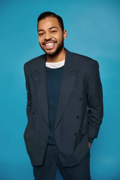 Heureux afro-américain jeune homme en tenue bleu foncé souriant à la caméra avec les mains dans les poches — Photo de stock