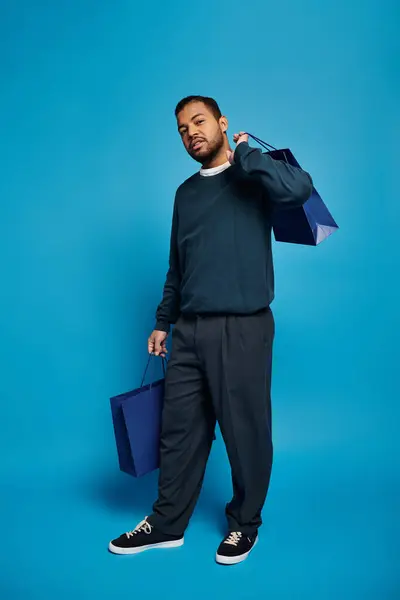 Afrikanisch-amerikanischer Mann im dunkelblauen Outfit posiert mit Einkaufstaschen in der Hand vor lebendigem Hintergrund — Stockfoto
