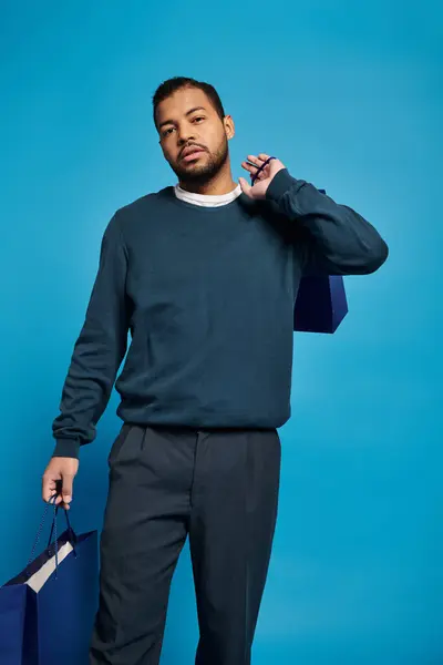 Attraktiver afrikanisch-amerikanischer Mann im dunkelblauen Outfit mit Einkaufstaschen in der Hand vor der Kamera — Stockfoto