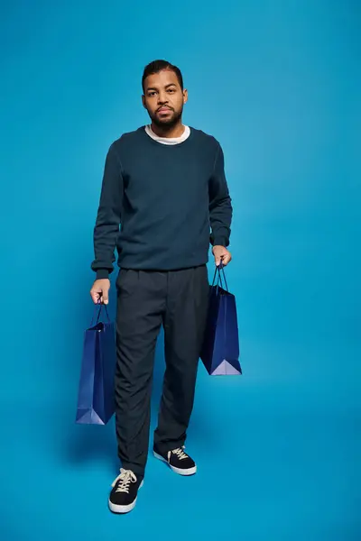 Handsome african american man walking with shopping bag in hands on blue background — Stock Photo