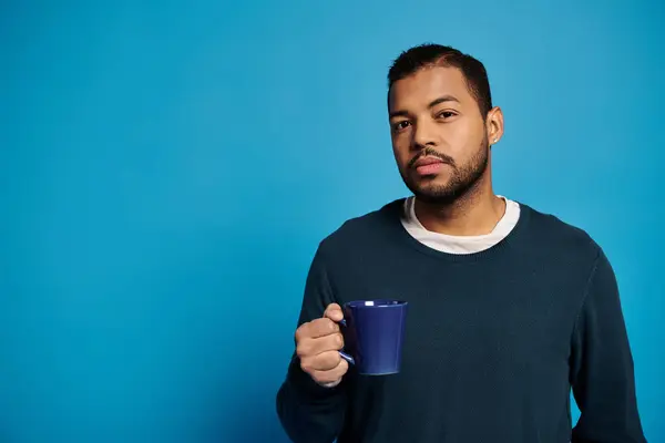 Portrait of attractive african american man in his 20s holding cup in hand against blue background — Stock Photo