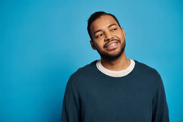 Happy and attractive african american man in his 20s looking to side against blue background — Photo de stock