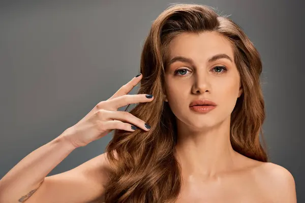 Uma jovem mulher com cabelos longos e ondulados posando em fundo cinza. — Fotografia de Stock