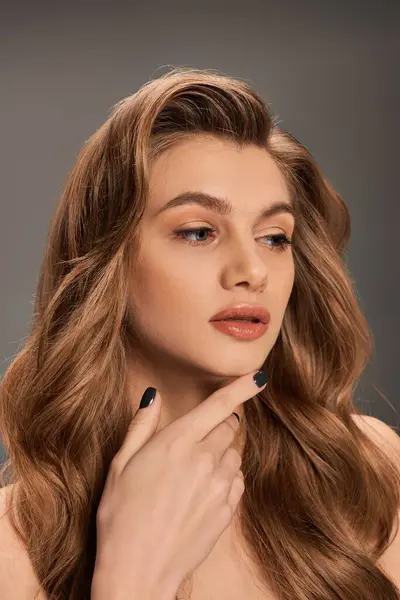 Eine atemberaubende junge Frau mit langen welligen Haaren posiert vor grauem Hintergrund. — Stockfoto