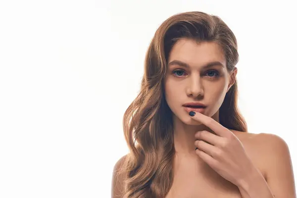 Une jeune femme aux cheveux longs et ondulés regardant la caméra sur fond gris — Photo de stock