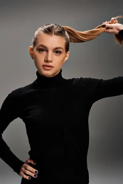 Eine junge, schöne Frau in einem schwarzen Top hält anmutig ihr langes Haar und präsentiert Eleganz und Stil. — Stockfoto