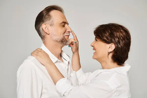 Retrato de casal sorridente de meia-idade, mulher tocando o nariz do homem em fundo cinza — Fotografia de Stock