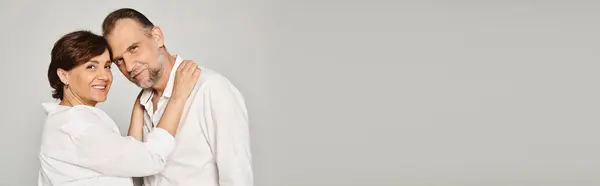 Portrait of middle aged smiling couple hugging and looking at camera on grey background, banner — Stock Photo