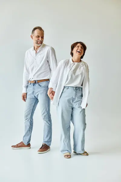 Ältere schöne Paar in der Liebe lachen und stehen auf grauem Hintergrund und Händchen halten — Stockfoto