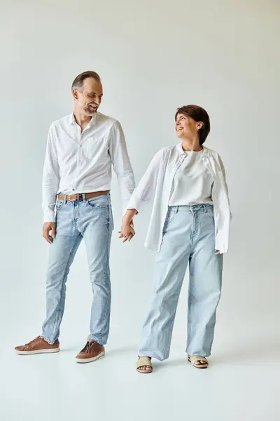 Pieno colpo di coppia matura innamorata sorridente e in piedi su sfondo grigio e tenendosi per mano — Foto stock