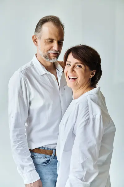 Mature couple in love smiling and standing on grey background, woman looking at camera — Stock Photo