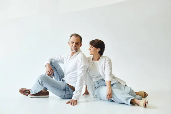 Middle aged beautiful couple sitting on grey background and looking at each other, love — Stock Photo
