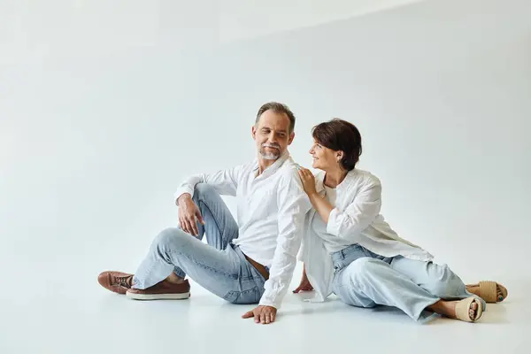 Tiro de comprimento total de casal bonito maduro sentado no fundo cinza e olhando um para o outro — Fotografia de Stock