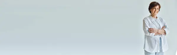 Mujer alegre de mediana edad de pie con los brazos cruzados y mirando a la cámara con sonrisa, pancarta - foto de stock