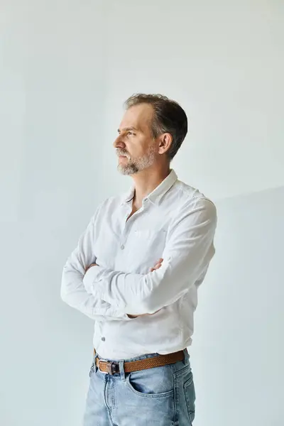 Portrait of mature handsome man in white shirt standing with his arms crossed and looking away — Stock Photo