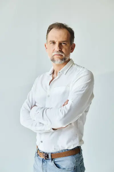 Retrato de hombre guapo maduro en camisa blanca de pie con los brazos cruzados y mirando a la cámara - foto de stock